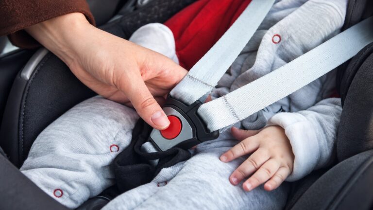 Adult hand checking a child car seat harness buckle